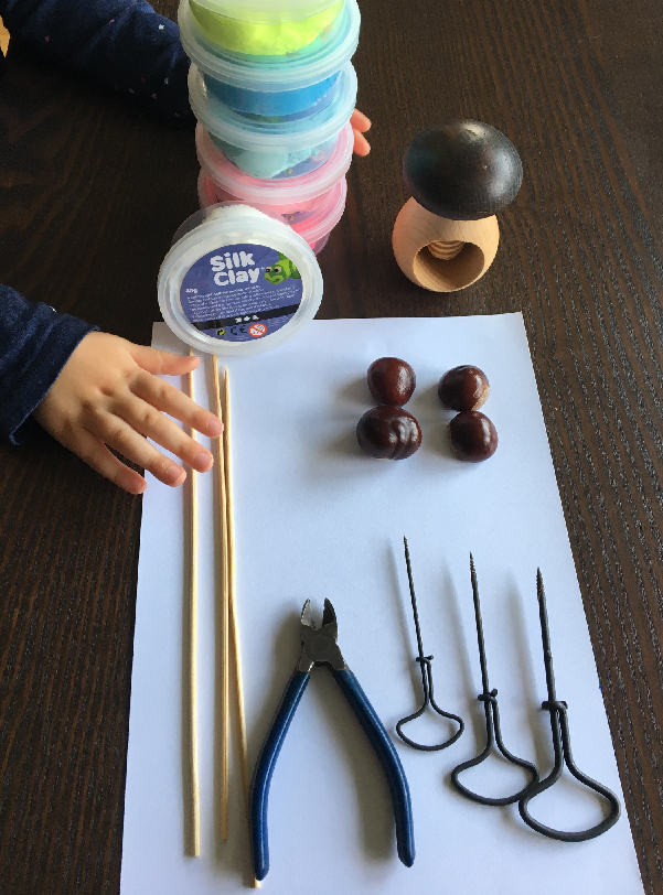 Bastelmaterial auf dem Tisch: Silk Clay, Haltepilz, Kastanien, Holzspieße, Seitenschneider und drei Kastanienbohrer