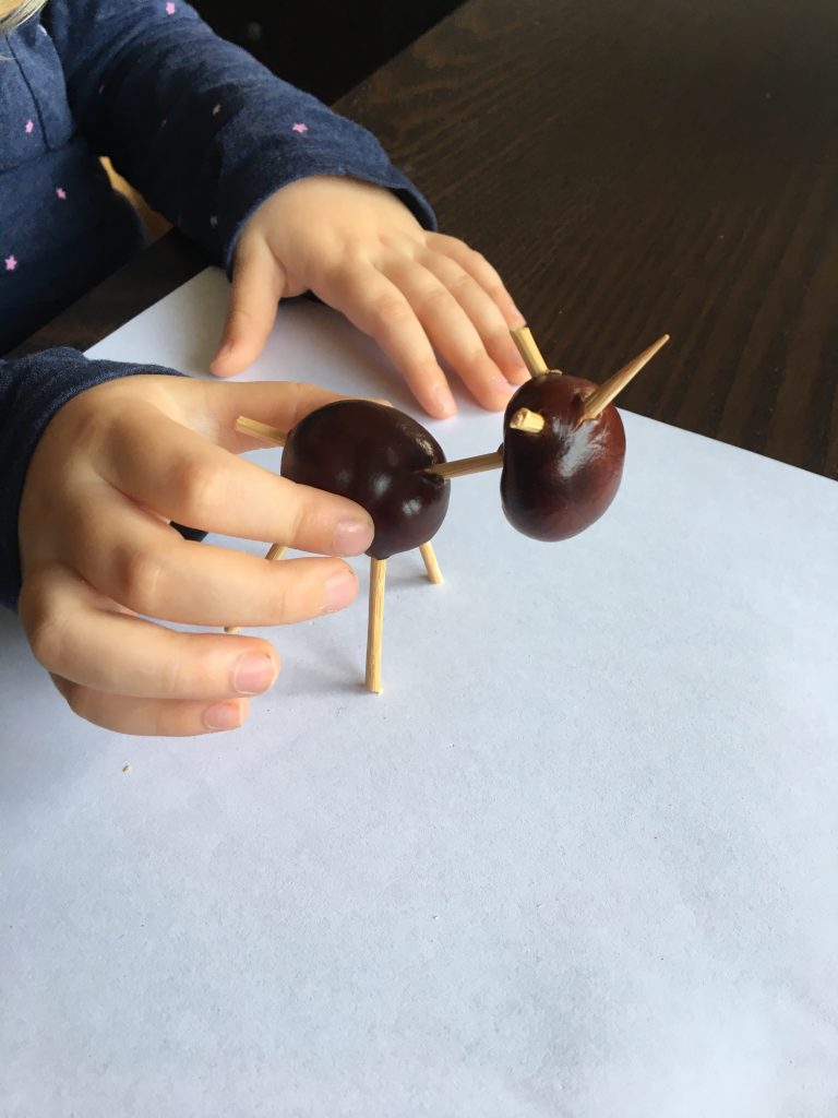 Kinderhände halten das Gerüst, am Kopf stecken Stäbchen für Ohren und Horn