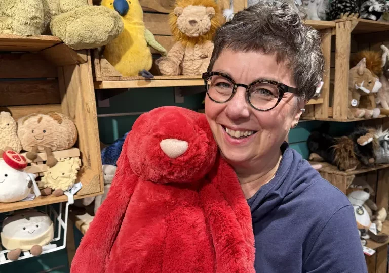 Mitarbeiterin von Salima hält ein großes rotes Jellycat-Kuscheltier vor dem Regal mit weiteren Kuscheltieren
