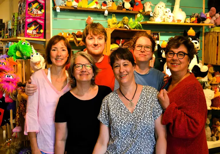 Das Team von Salima Kinderschätze: sechs Menschen im Laden vor Regalen voller Kuscheltiere und Handpuppen