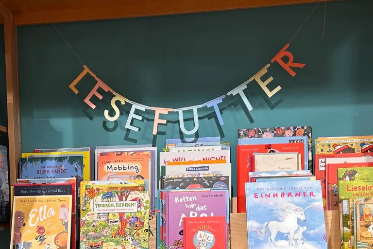 Bücherwand bei Salima unter der Girlande „Lesefutter“ mit Bilderbüchern wie „Ella“, „Tierisch, tierisch!“ und „Das geheime Leben der Einhörner“